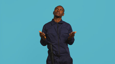 Security guard tasked with restricting unwanted access looking to sky, praying. Portrait of bodyguard waiting for miracle, doing spreading arms gesture, studio background, camera Bの写真素材