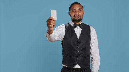 Classy hotel bellboy in tuxedo giving the room access key card to guest after check in, offering excellent concierge services at holiday resort. Employee working in hospitality industry. Camera B.の写真素材
