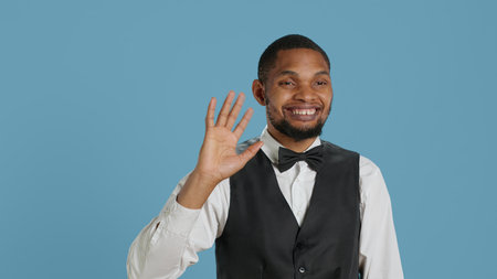 Bellboy employee smiling and waving hello at hotel guests, greeting people with confidence and offering luxury services for a pleasant stay. Cheerful personnel saying hi to people. Camera A.の写真素材