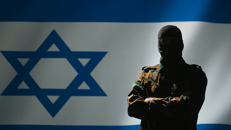 Mossad operator wearing mask to remain anonymous standing proud in front of Israel flag, feeling pride in serving country. Israeli secret agent in command room crossing arms, camera Bの写真素材