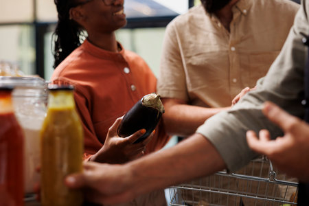 Multiethnic people carrying eco friendly groceries at a local convenience store. Close-up of smiling black woman holding a fresh grown eggplant fruit at a bio food organic shop.の写真素材