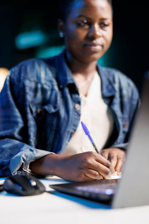A multitasking African American woman working from home, using her laptop to research and review...