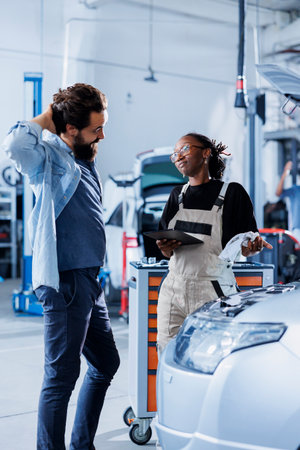 Client shocked by price after repairman in car service uses tablet to calculate invoice for repaired fuel tank. Garage specialist surprising man with final costs after servicing his vehicleの写真素材