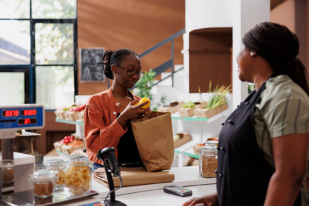 African American woman vendor at a small grocery store with a female customer, promoting healthy and...