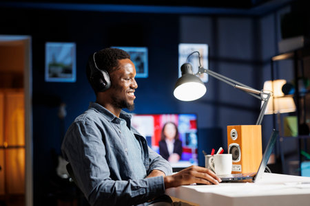 Employee listening to podcast at home and working on new plan, solving his responsibilities with new freelance contract terms. African american freelancer studying executive information online.の写真素材