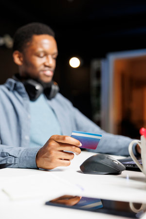 African american man entering card numbers on website, preparing to pay for clothes order on online store. Young adult uses electronic banking transaction during shopping session on laptop.の写真素材