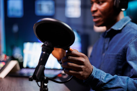 Black man using a professional microphone to record podcast in home studio. Closeup of african american male individual touching modern condenser mic and speaking into it, doing radio program.の写真素材