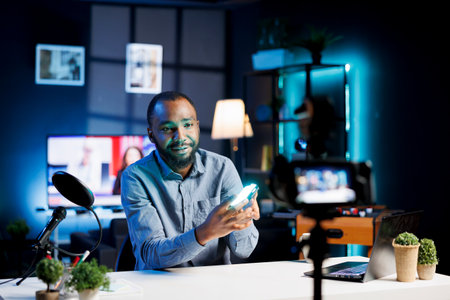 Smiling online show host being sponsored by partnering brand to do mini RGB lights unboxing content. Man does influencer marketing, doing product placement of video production toolの写真素材