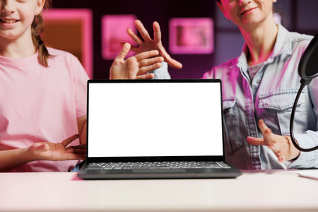 Entertaining child and mom filming video assessing mockup laptop performance, talking about components used. Daughter and parent shoot isolated screen notebook device review for internet channelの写真素材