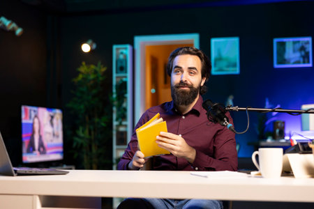 Man working on audiobook recording production, reading from book and capturing sound with professional microphone. Voice actor producing online ebook content for internet publishersの写真素材