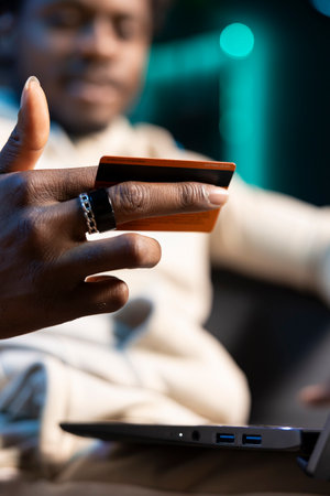 Close up shot of debit card in man hand adding payment method on website, relaxing in cozy home....