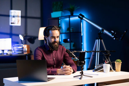 Online star talking in front on smartphone attached to tripod and high quality mic in studio,...