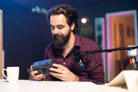 Tech content creator filming technology review of newly released V mount battery, unpacking it and presenting specifications to audience. Influencer showing charging device to subscribersの写真素材