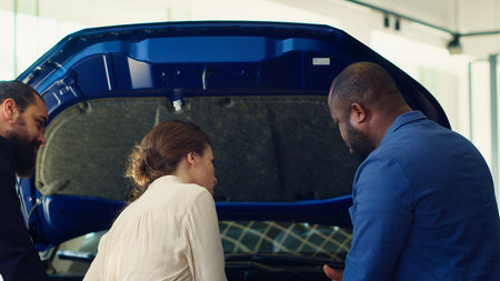 Dealership salesman answering customers questions about cars, showing parts used. Showroom agent...