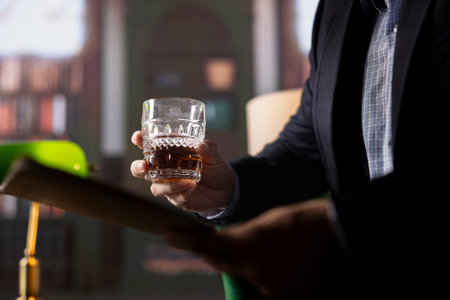 Enforcement agent sharing crucial insights to his colleague, enjoying glasses of whiskey in the safe house library. Government spies meeting over drinks to discuss evidence analysis. Close up.の写真素材