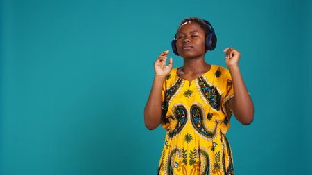Carefree relaxed woman listening to music and dancing in the studio, having fun with a new groovy playlist. Happy optimistic person enjoys radio songs on her audio headset. Camera B.の写真素材