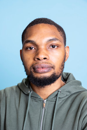 Portrait of african american guy wearing a grey hoodie and smiling, posing in front of the camera...