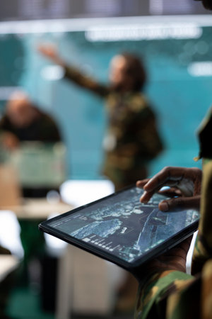 Army staff monitoring infantry unit on ongoing operation using his tablet, using surveillance radar system and a world map. IT professional working with reconnaissance gear. Close up.の写真素材
