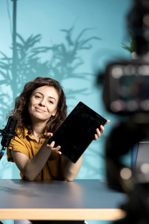 Happy entertaining woman in studio films tablet video review for tech enthusiasts. Joyous online...