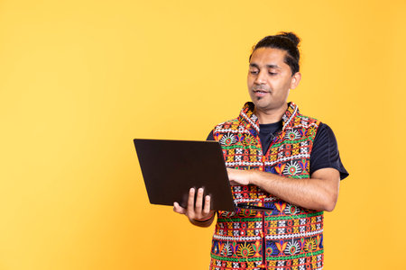 Indian man typing on laptop keyboard, doing job tasks for company, isolated over studio background. Worker inputting data on notebook device, working as office clerk, studio backdropの写真素材