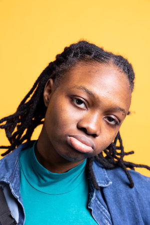 Portrait of stern teenager posing, isolated over yellow studio background, close up shot. BIPOC...