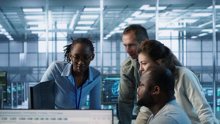 Multiethnic team of engineers working in server hub, using PCs to analyze data. Multiracial group of...