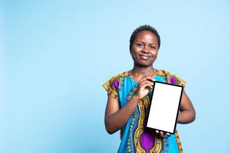 Confident woman showing tablet with blank mockup layout, creating advertisement with isolated copyspace template on wireless device. African american girl presents white display on camera.の写真素材