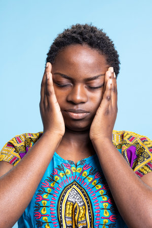 African american woman having signs of the flu and a terrible headache in the studio. Young person dealing with a medical problem, unpleasant migraine is making her feel miserable.の写真素材