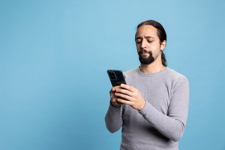 Tech savvy individual holding a phone against a blue background, conveying calm and professionalism. Cool natural guy illustrating online work, digital engagement or networking in the digital world.の写真素材