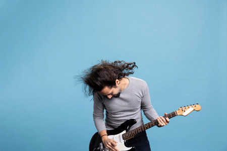 Enthusiastic rocker playing a black electric guitar with passion and joy for rock and roll music. Dynamic, trendy performer with long hair brings movement, fun and entertainment to the studio.の写真素材
