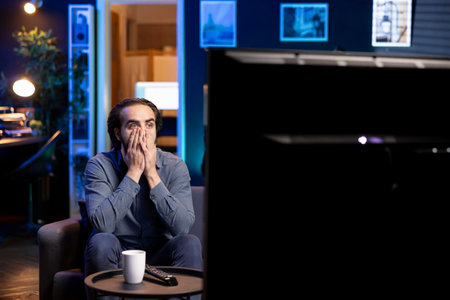 Shocked fan watching live sports event on TV in living room, unable to believe eyes seeing favorite...