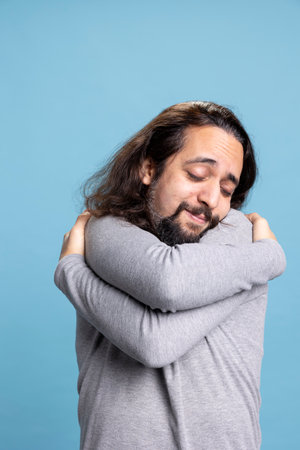 Happy person feeling fulfilled and embracing himself as a form of self love, showing self appreciation and a powerful personality against blue background. Young adult relaxed and confident.の写真素材