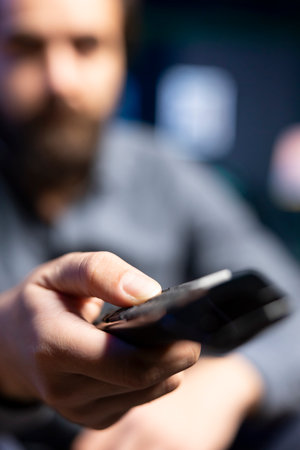 Focus on remote control used by man in blurry background to select movie on streaming services, having relaxing evening. Viewer in apartment changing channels on TV set, close up shotの写真素材