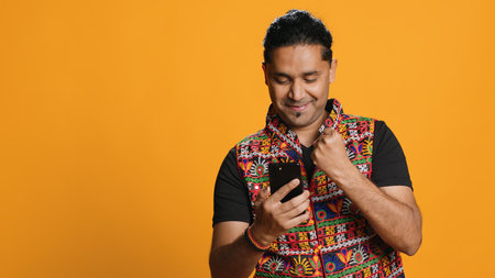 Happy man playing videogames on smartphone, celebrating after defeating foes, doing clenching hand gesture. Player swiping phone screen, thrilled about winning game, studio background, camera Aの写真素材