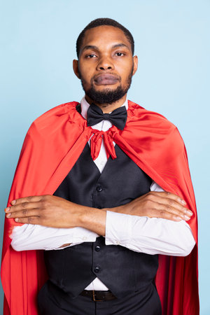 African american doorman posing in a superhero red mantle in studio, acting as a hero and savior for the clients. Happy confident bellhop with a superhuman cape, professionalism.の写真素材