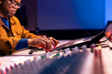 Audio engineer producing new tracks on console in control room, twisting knobs and pressing faders...