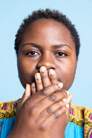 African american woman covering her mouth in front of the camera, being silent and recreating three...