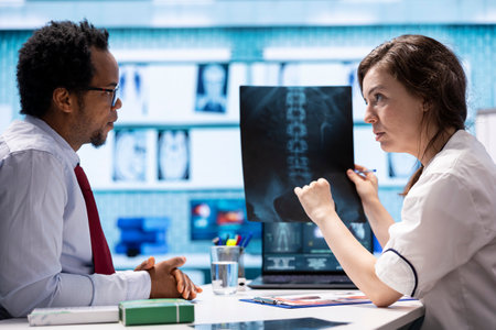 Professional medic presenting the diagnostics for male patient in office, discussing about radiography test findings and lab analysis. Doctor offering treatment on insurance, medical services.の写真素材