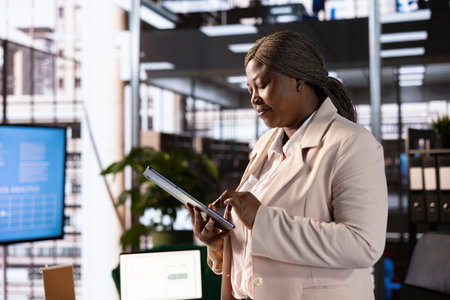 Businesswoman using tablet to analyze market trends and data in office. Entrepreneur developing trading strategies and algorithms, checking paperwork on electronic deviceの写真素材