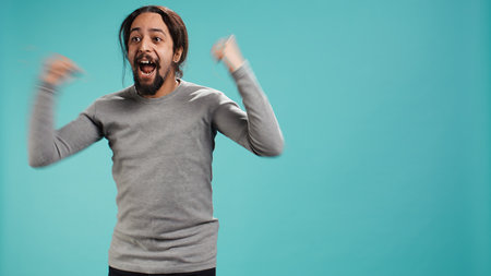Man jumping from joy in excitement while cheering for favorite sports team, studio background. Person celebrating after victory, showing intense enthusiasm, supporting team during game, camera Bの写真素材