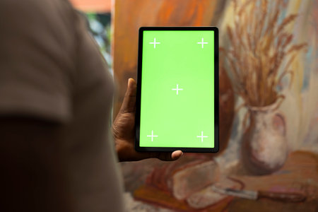 African american artist holding device with green screen mockup in art studio, working on a new painting with a certain technique. Painter using watercolor and acrylic dye for his creation.の写真素材