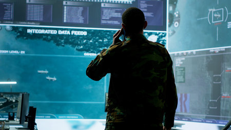 Military man answers phone call in a mission control center, working with advanced technology and satellite imagery to track potential threats and real time data. Intelligence activities. Camera A.の写真素材