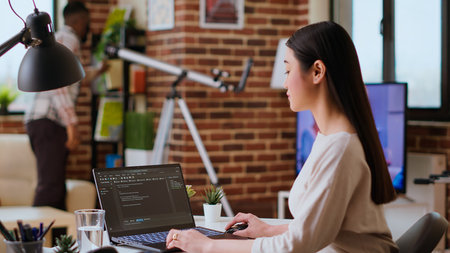 Asian freelancer woman works on programming code in a modern office at home, using her laptop for...