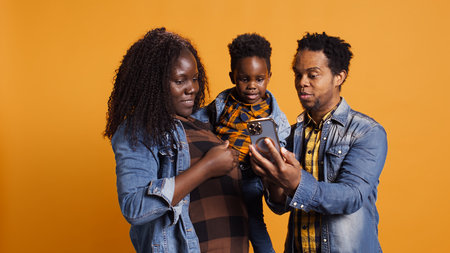 Cute happy family with a young kid take pictures on smartphone, carrying their son and sharing...