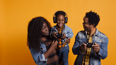 Joyful optimistic dad playing online video games with his boy using controller, parents enjoying leisure time with their small child. African american happy family play together in studio. Camera B.の写真素材