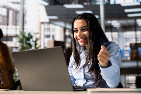 Joyful indian entrepreneur celebrates her work accomplishment and business win, thrilled with the successful outcome of her project development. Satisfied woman enjoys career growth.の写真素材