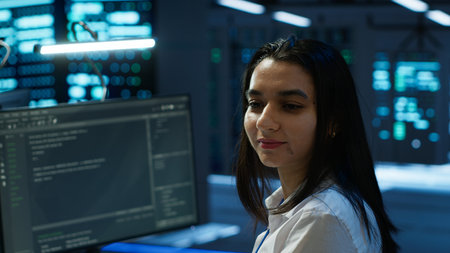 Portrait of cheerful engineer in data center installing software on computer, troubleshooting issues. Smiling IT specialist in server room establishing performance benchmarksの写真素材