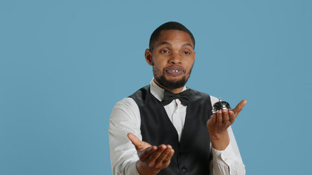 Bellhop doorkeeper ringing the service bell to present his help and assistance upon the guests arrival, blue background. Hotel porter providing great luxury services at resort. Camera A.の写真素材