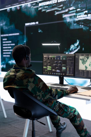 Army specialist working with advanced computer systems and cctv data for surveillance missions, gather intelligence to protect national interests. Strategic planning in a high tech control room.の写真素材