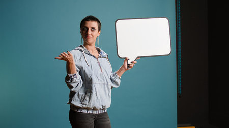 Female model with a groovy style holding a speech bubble in studio. Cool edgy woman presenting a...